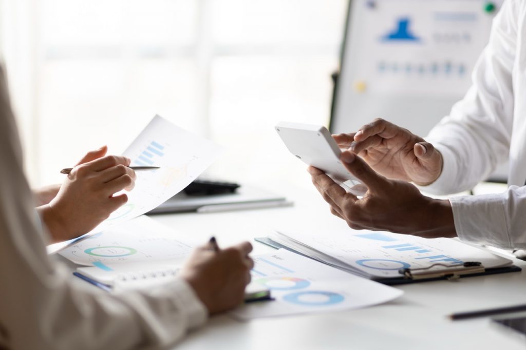 Business consulting meeting is discussing analysis financial data and business growth charts to plan strategy for generating company profits. Discuss cost budget analysis and plan to increase profits.